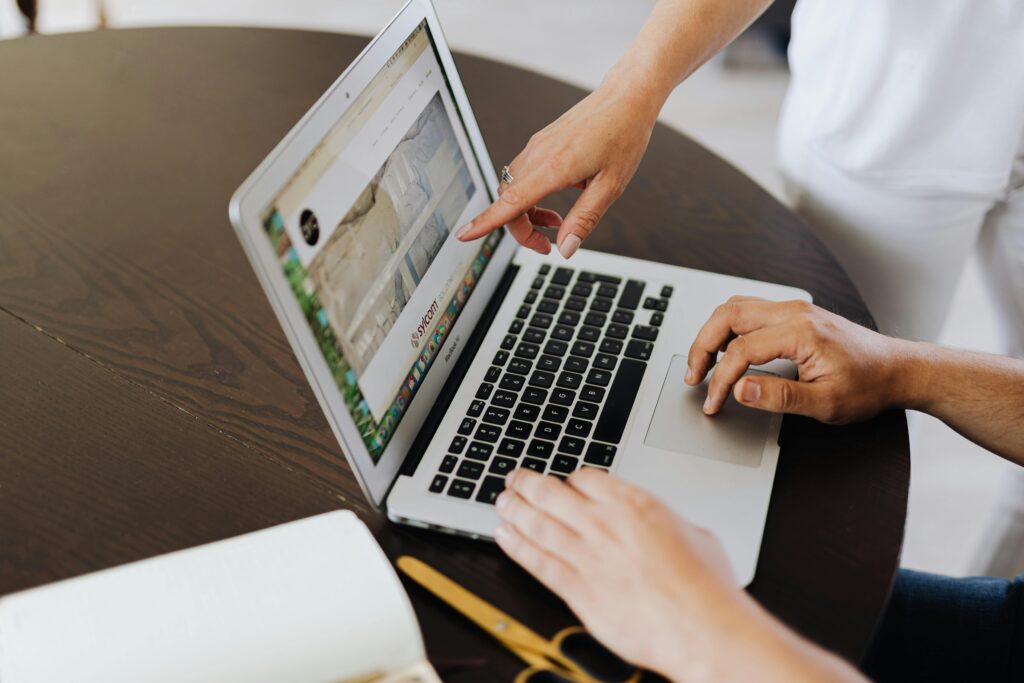 Two people collaborating on a laptop, engaged in a teamwork session at an office table.